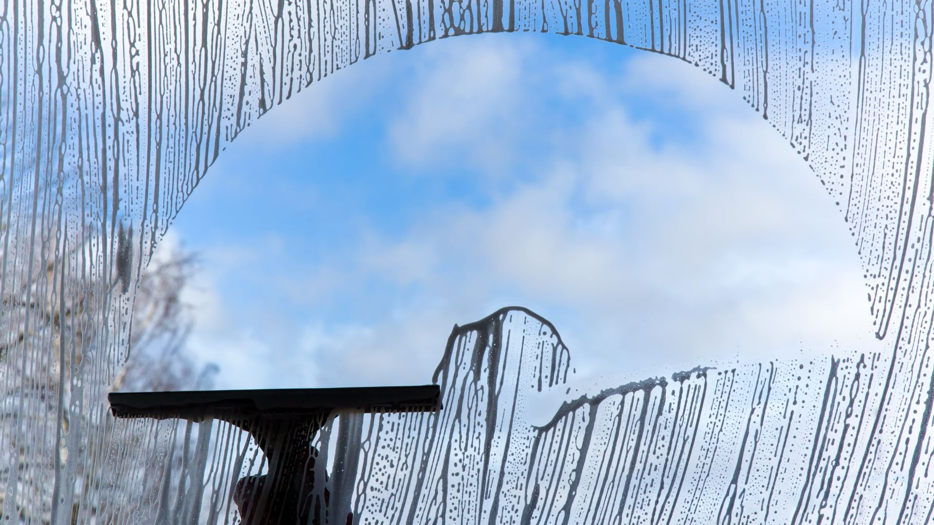 Squeegee cleaning wet window with blurry blue sky background