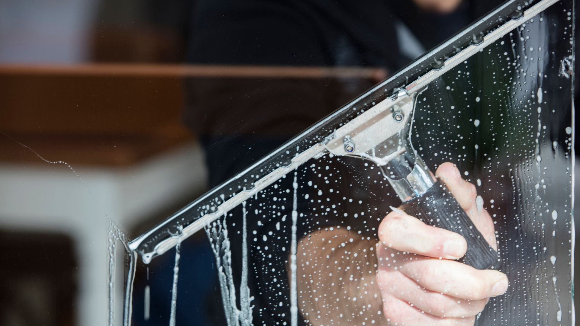 Hand cleaning window with squeegee, water droplets visible