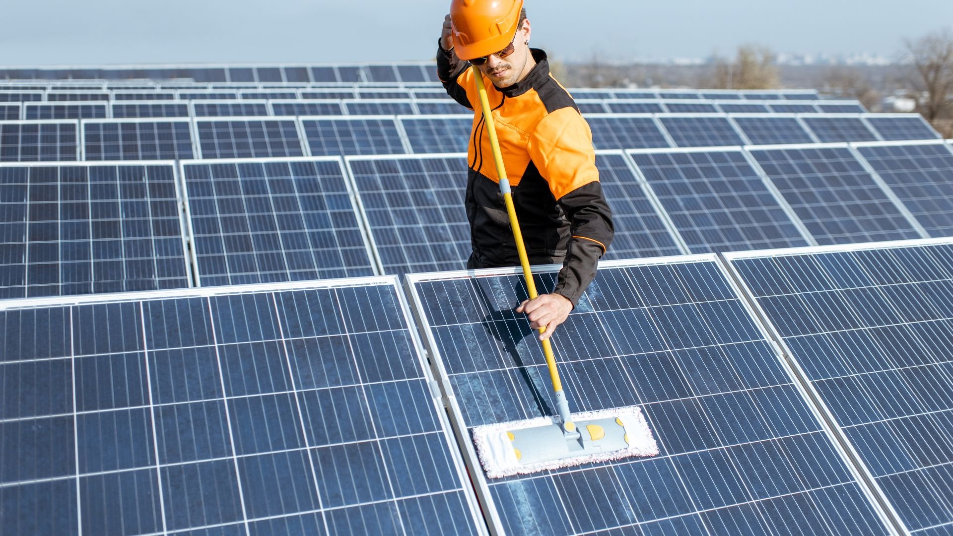 Worker in safety gear cleaning solar panels on a large solar farm