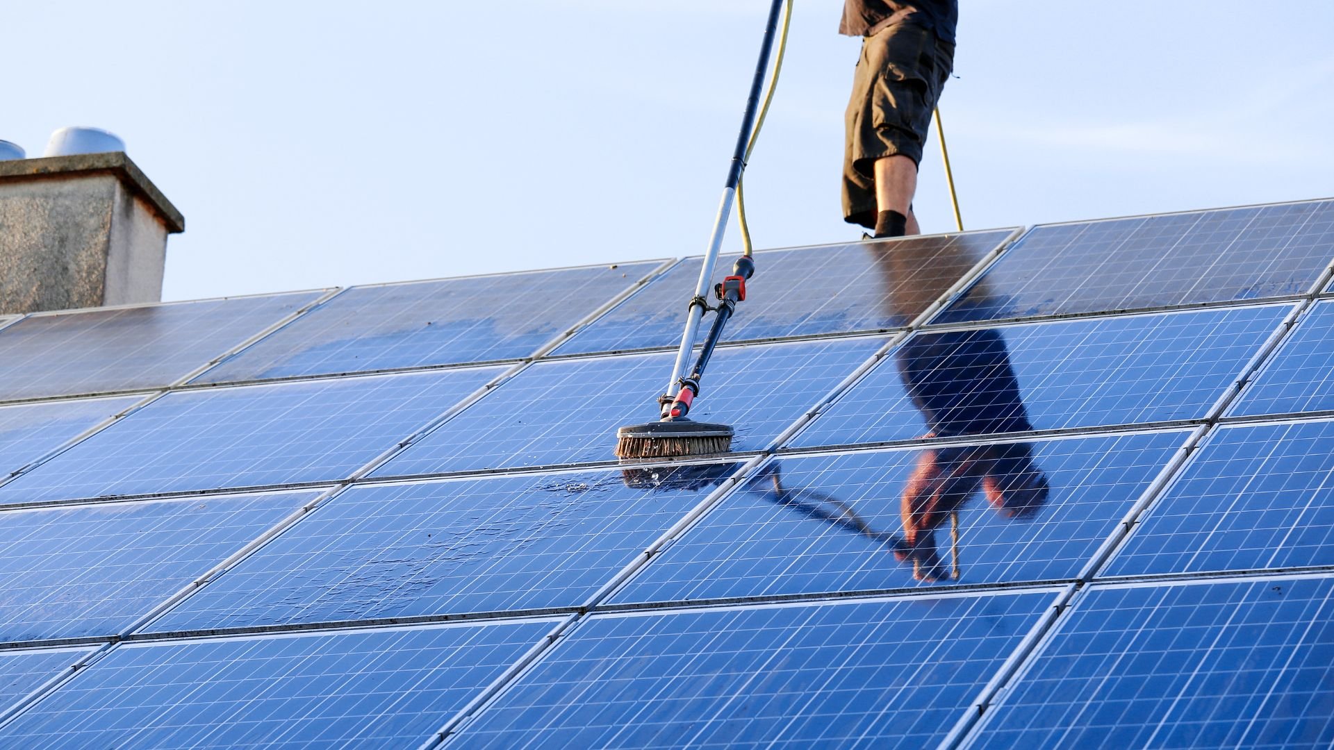 Worker cleaning solar panels on rooftop with long-handled brush